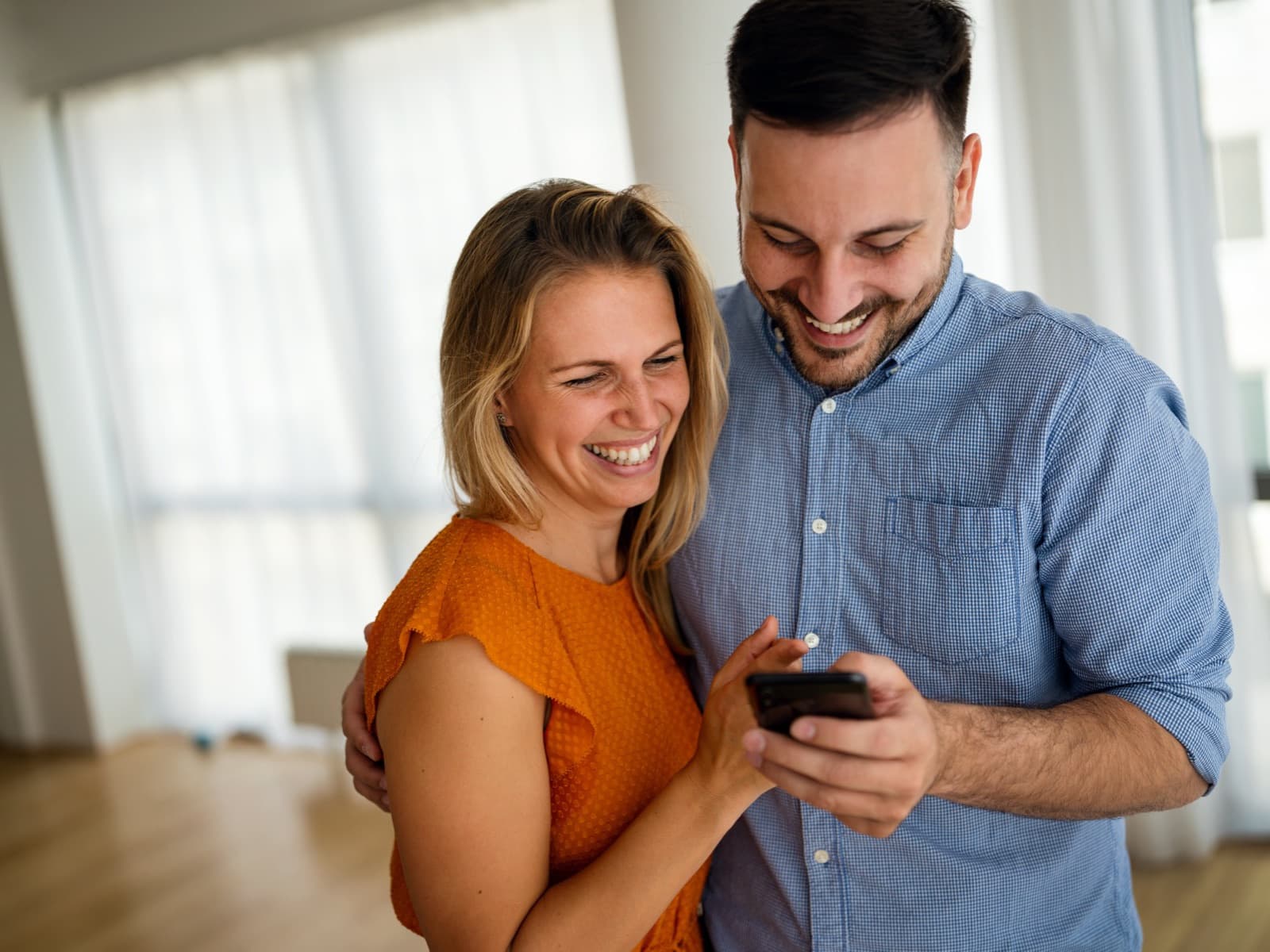Couple laughing at phone indoors.